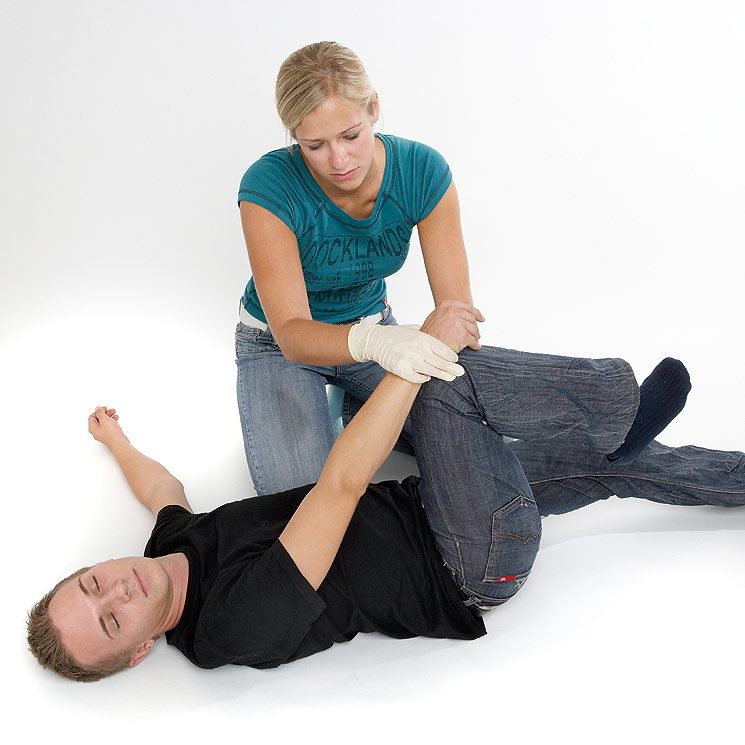 Dann mit einer Hand unter das gegenüberliegende Knie greifen und dieses anziehen; anschließend den gegenüberliegenden Arm zum Knie führen.